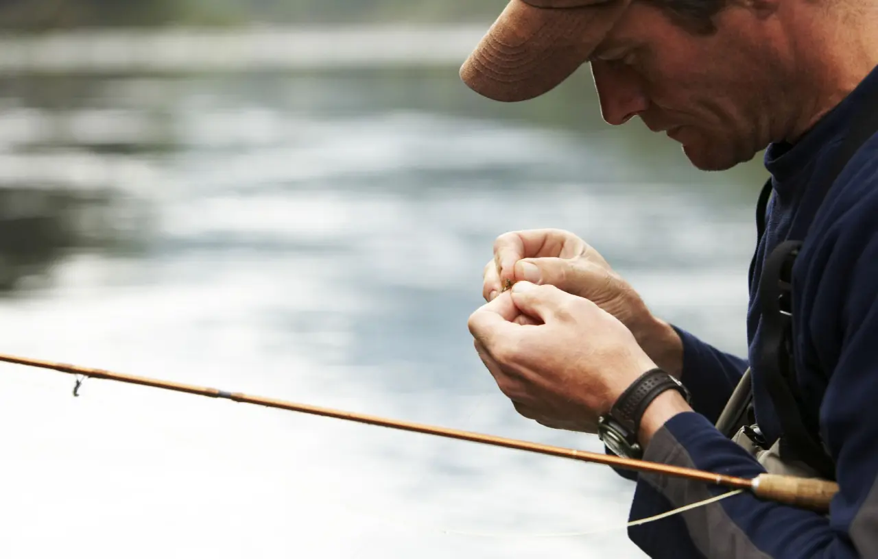 Man preparing fishing line by a river.