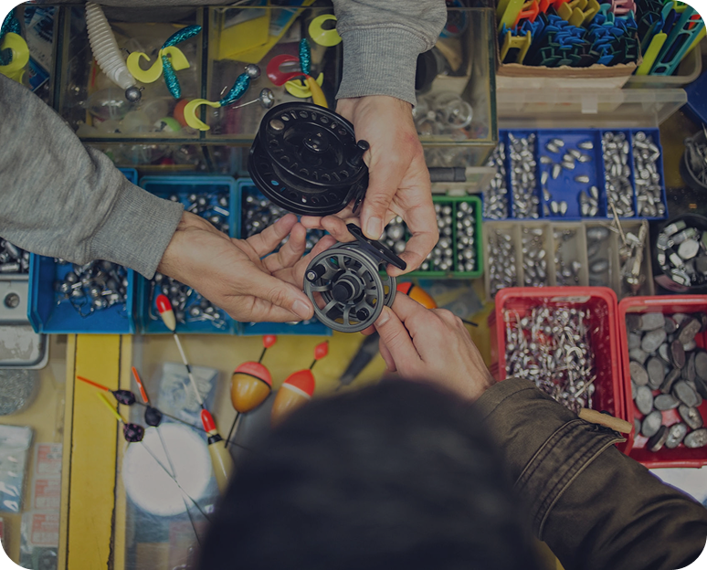 Hands inspecting fishing reel in tackle shop.