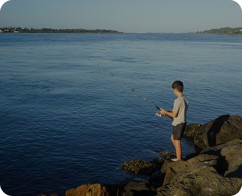Boy fishing by the rocky shoreline.